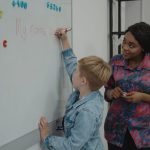 Mastering the First Impression: Your intriguing post title goes here A teacher helps a young student write on a whiteboard during a classroom lesson.